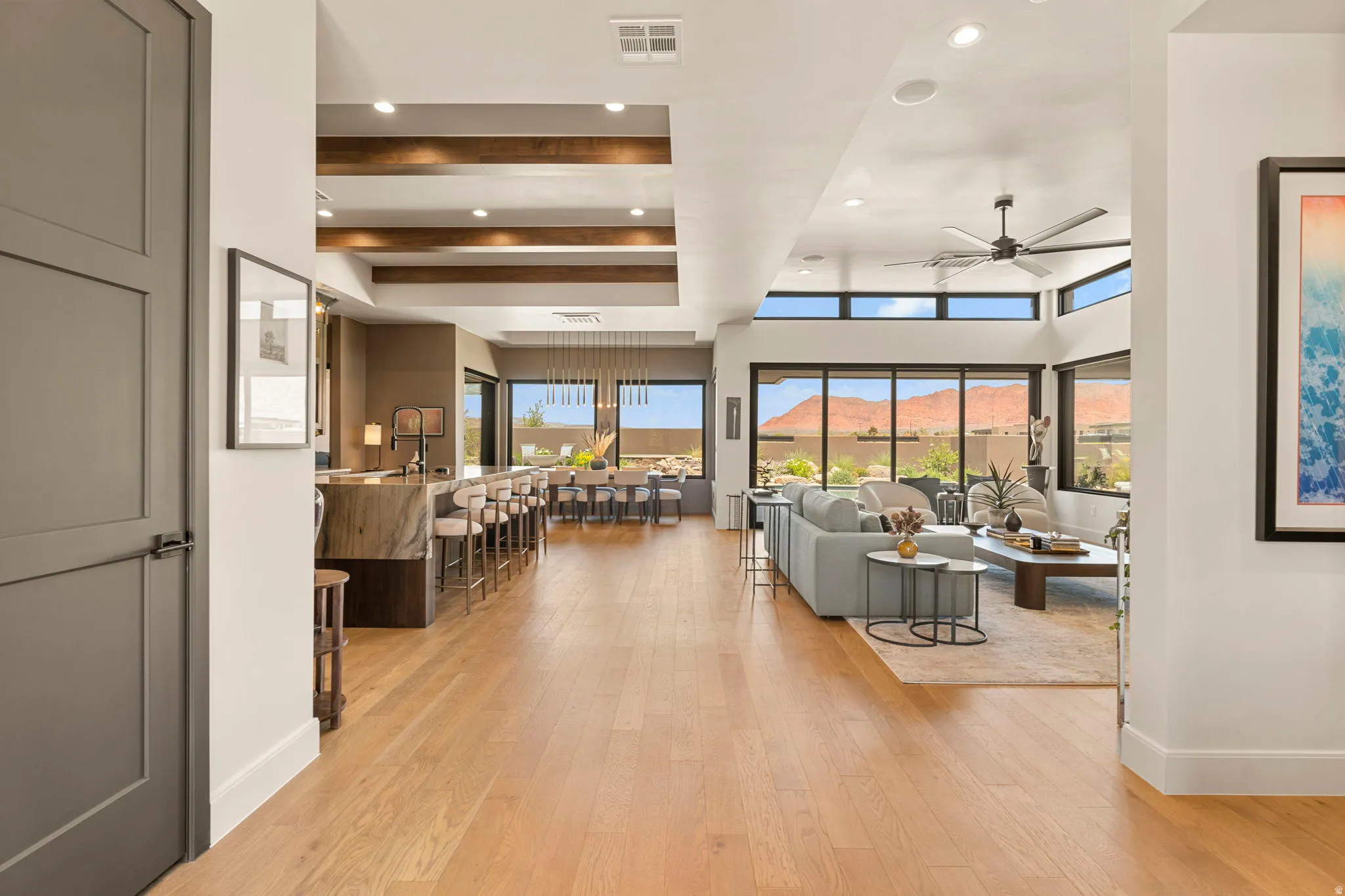Expansive living area featuring light hardwood flooring, exposed ceiling beams, and a contemporary ceiling fan