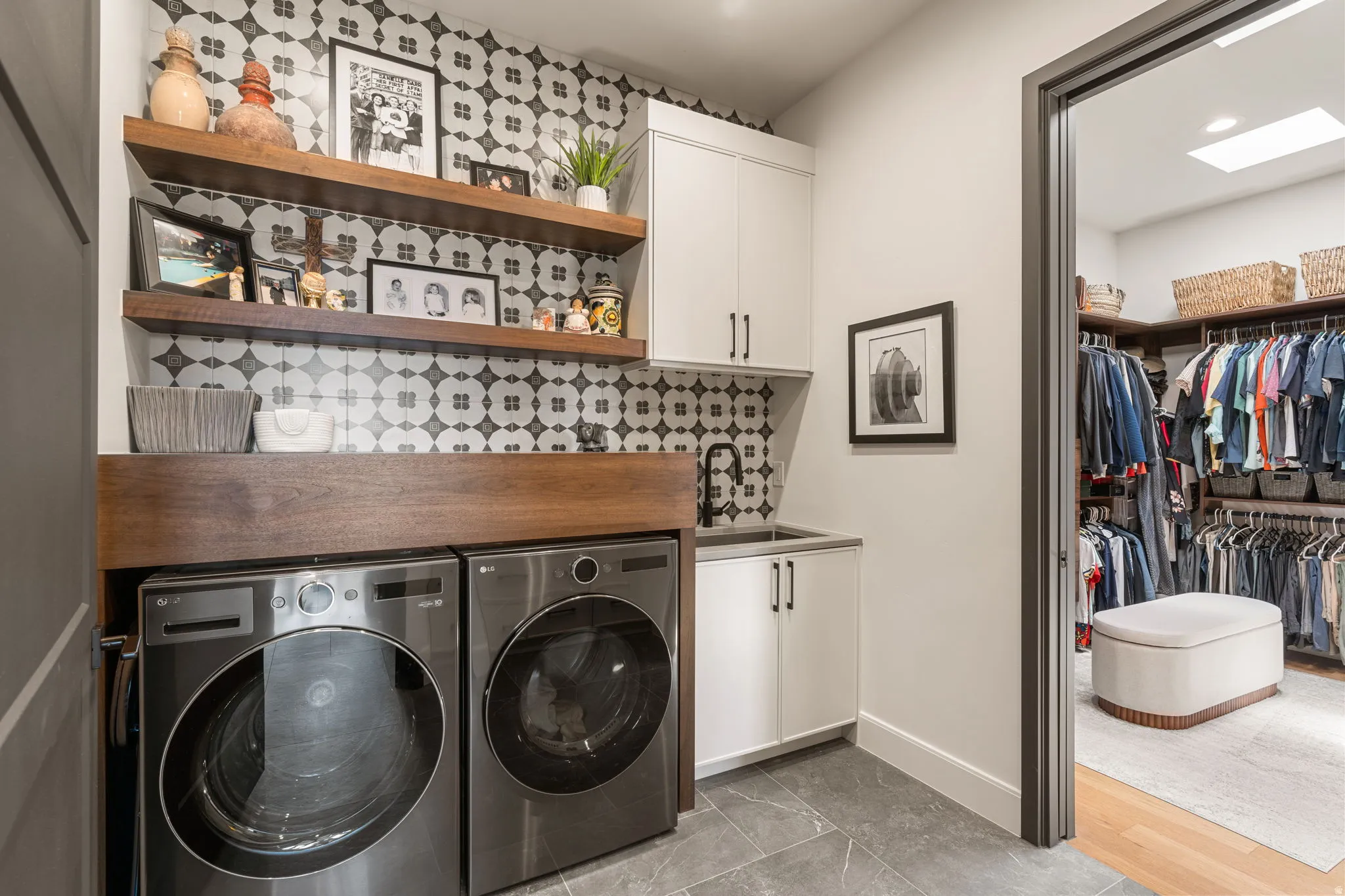 Laundry area featuring patterned tile backsplash, two open wood-finish shelves, and a utility sink with a black faucet