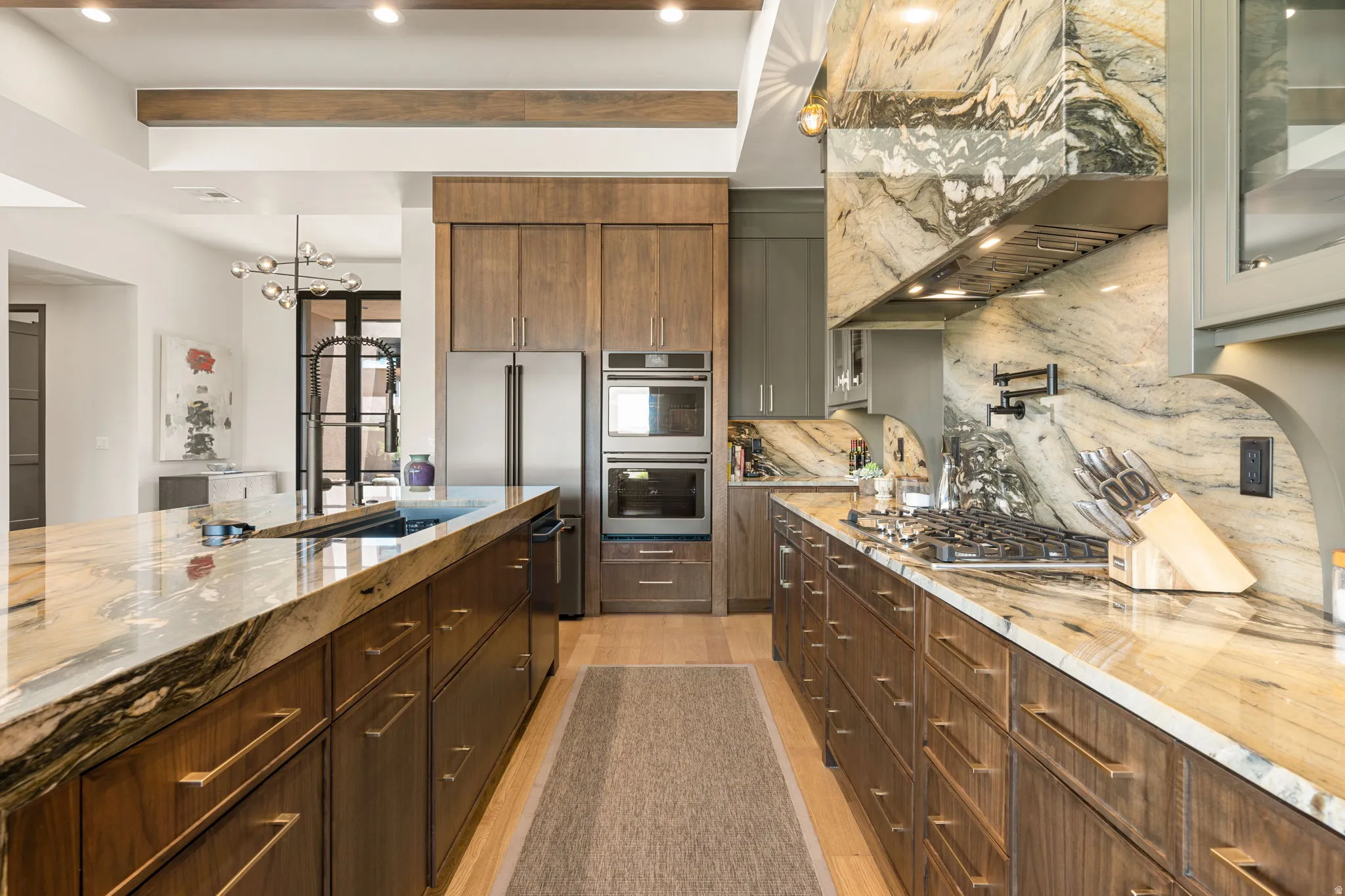 Gourmet kitchen featuring a natural stone waterfall island, integrated sink, gas range with pot filler, stainless steel appliances, and wood cabinetry