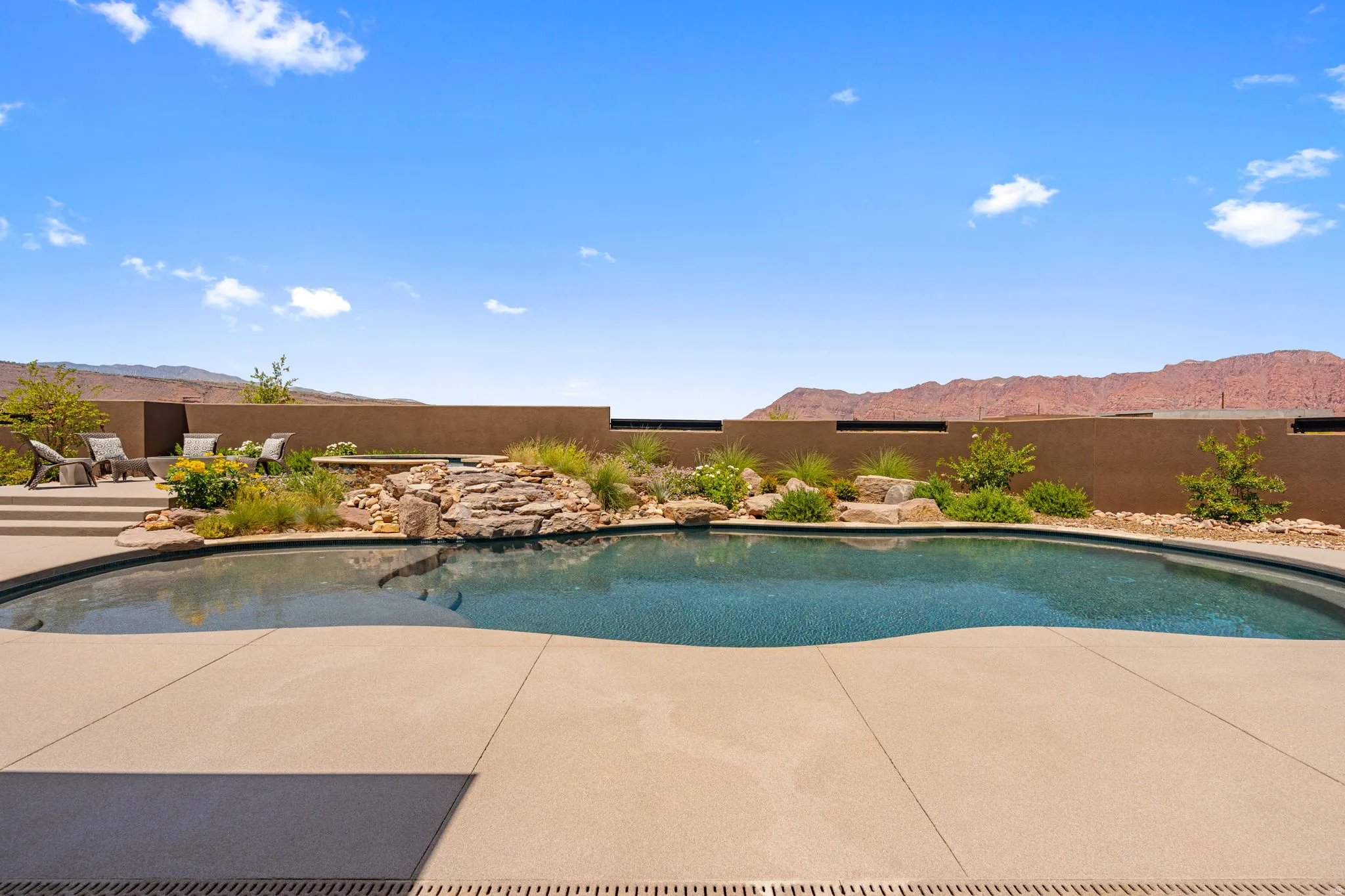 Freeform swimming pool with a rock waterfall feature, surrounded by concrete decking and desert landscaping