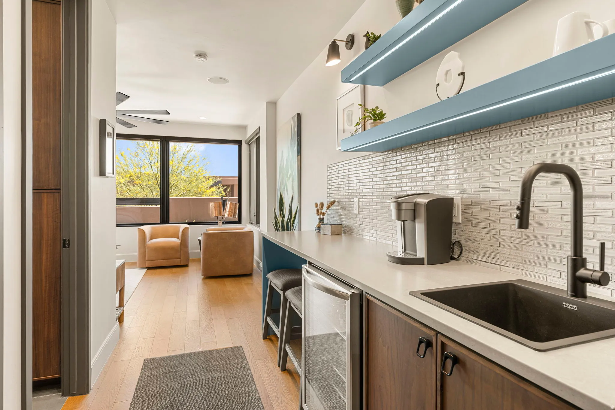 Casita featuring a beverage fridge, dark basin sink with a matte black gooseneck faucet, light-toned countertop, and mosaic tile backsplash