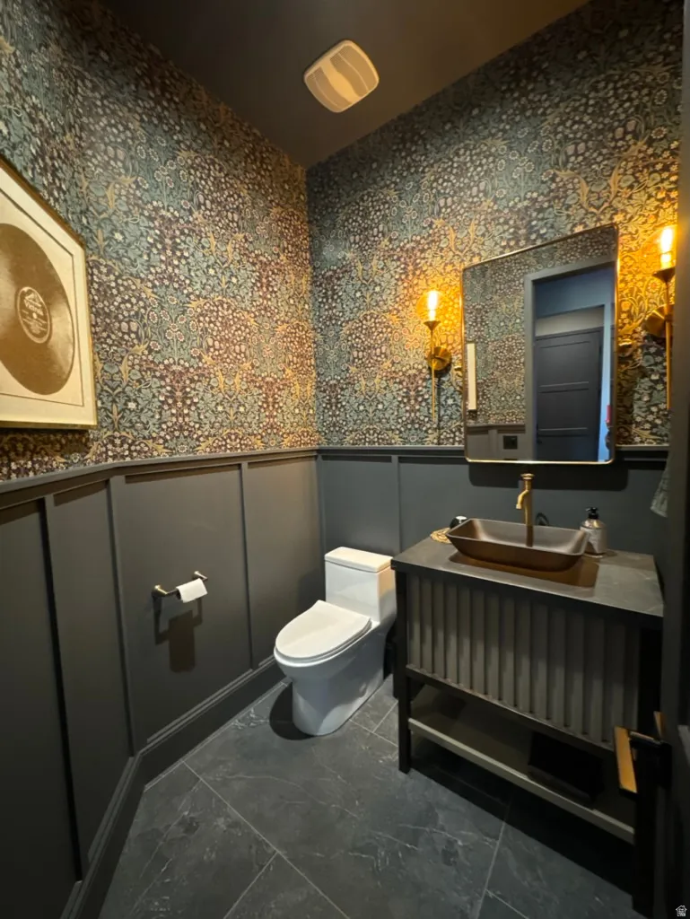Powder room featuring board and batten wainscoting, dramatic patterned wallpaper, wall-mounted sconces, a contemporary vanity with a vessel sink, and large format floor tiles