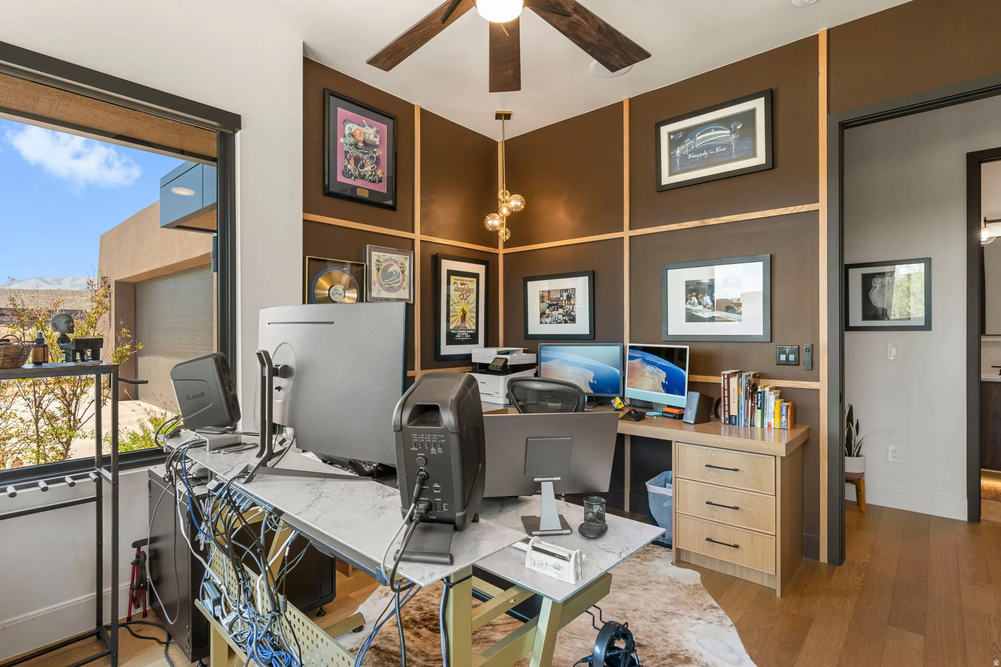 Room featuring a large window, a ceiling fan with integrated lighting, hardwood flooring, and accent walls with decorative paneling