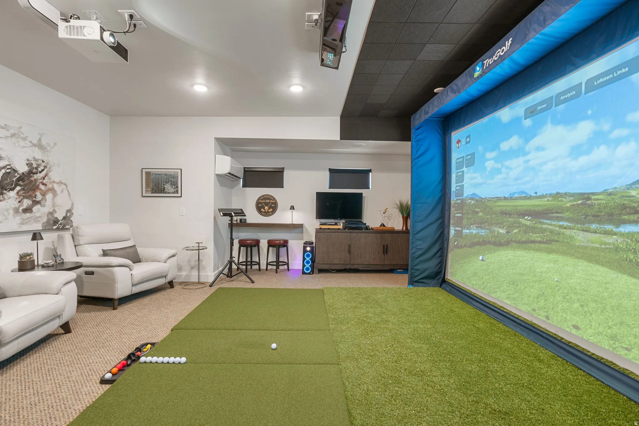Dedicated golf simulation area with artificial turf hitting mats and a large projection screen