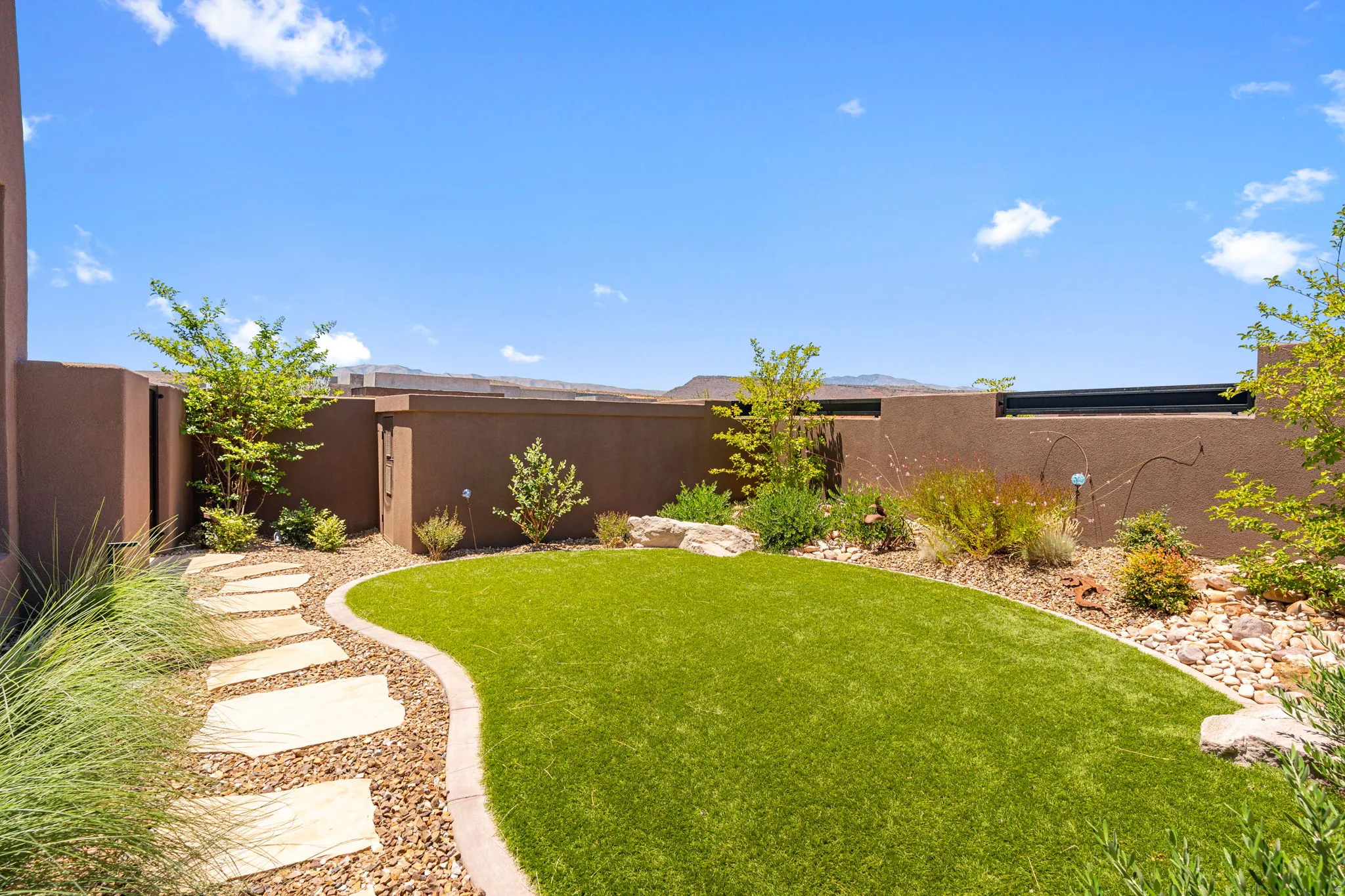 Private backyard featuring a curved artificial turf lawn, a flagstone path, enclosed pool equipment room and perimeter landscaping with mature shrubs and decorative rocks