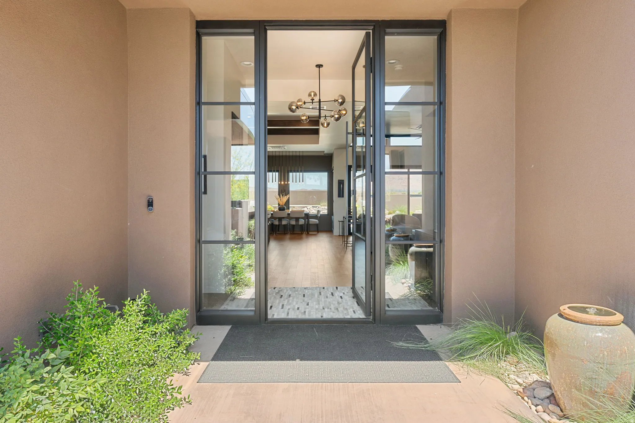 Double glass-paneled entry doors with dark framing, leading to an interior with hardwood flooring and a contemporary chandelier