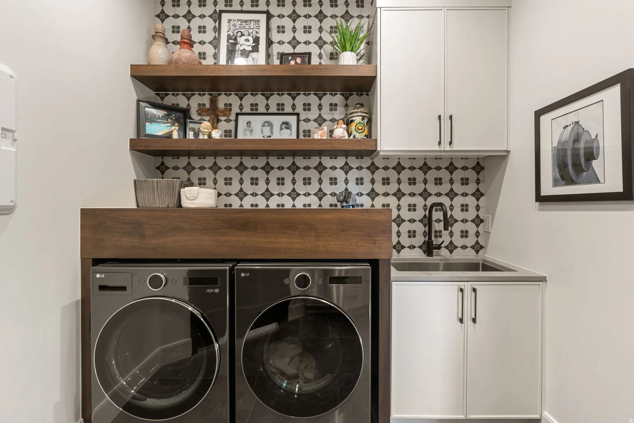 Laundry area featuring a patterned tile backsplash, wood-finish floating shelves, and white cabinetry