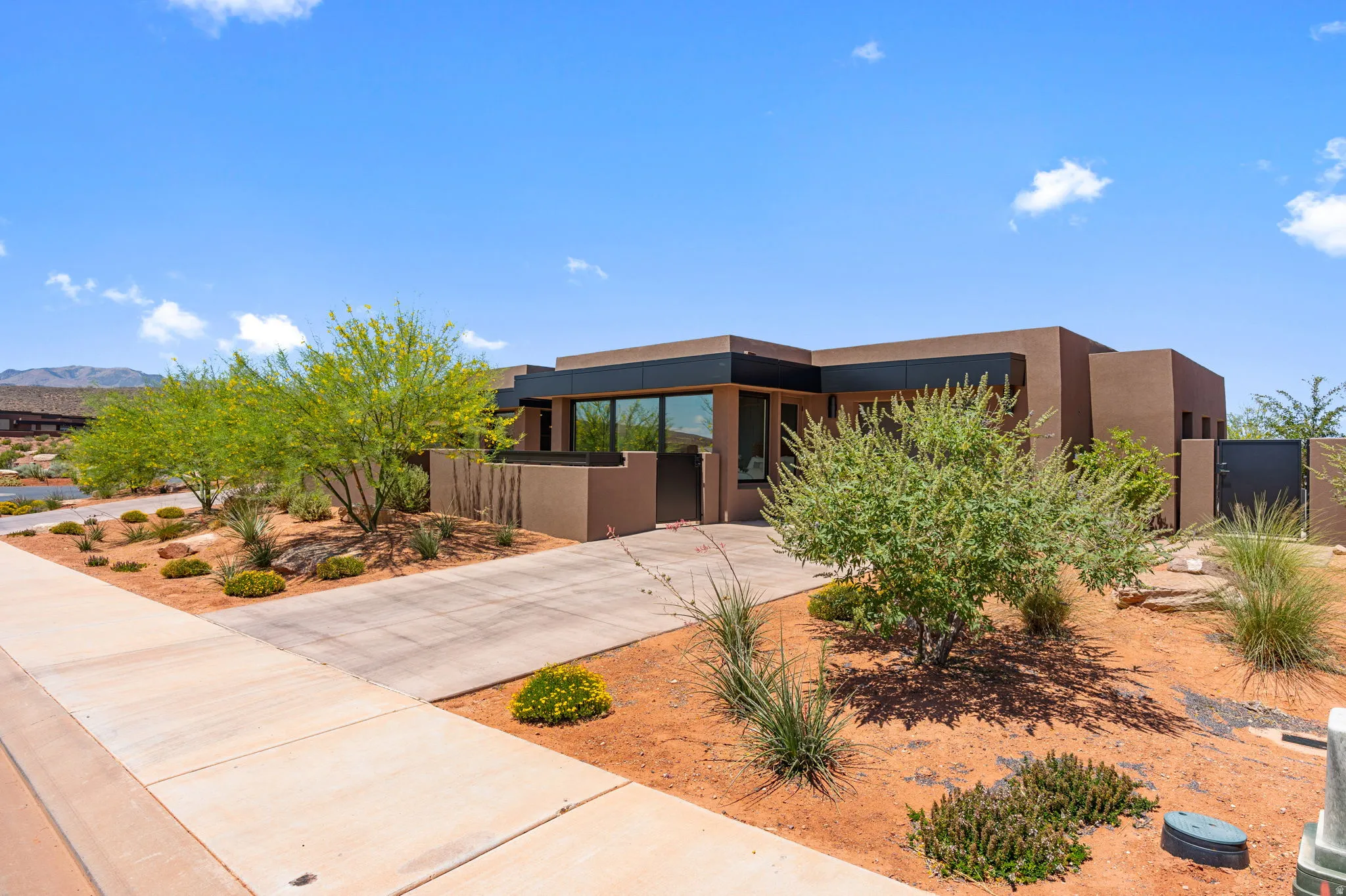 Contemporary desert-style residence featuring a stucco exterior, dark trim accents, expansive windows, and a concrete driveway