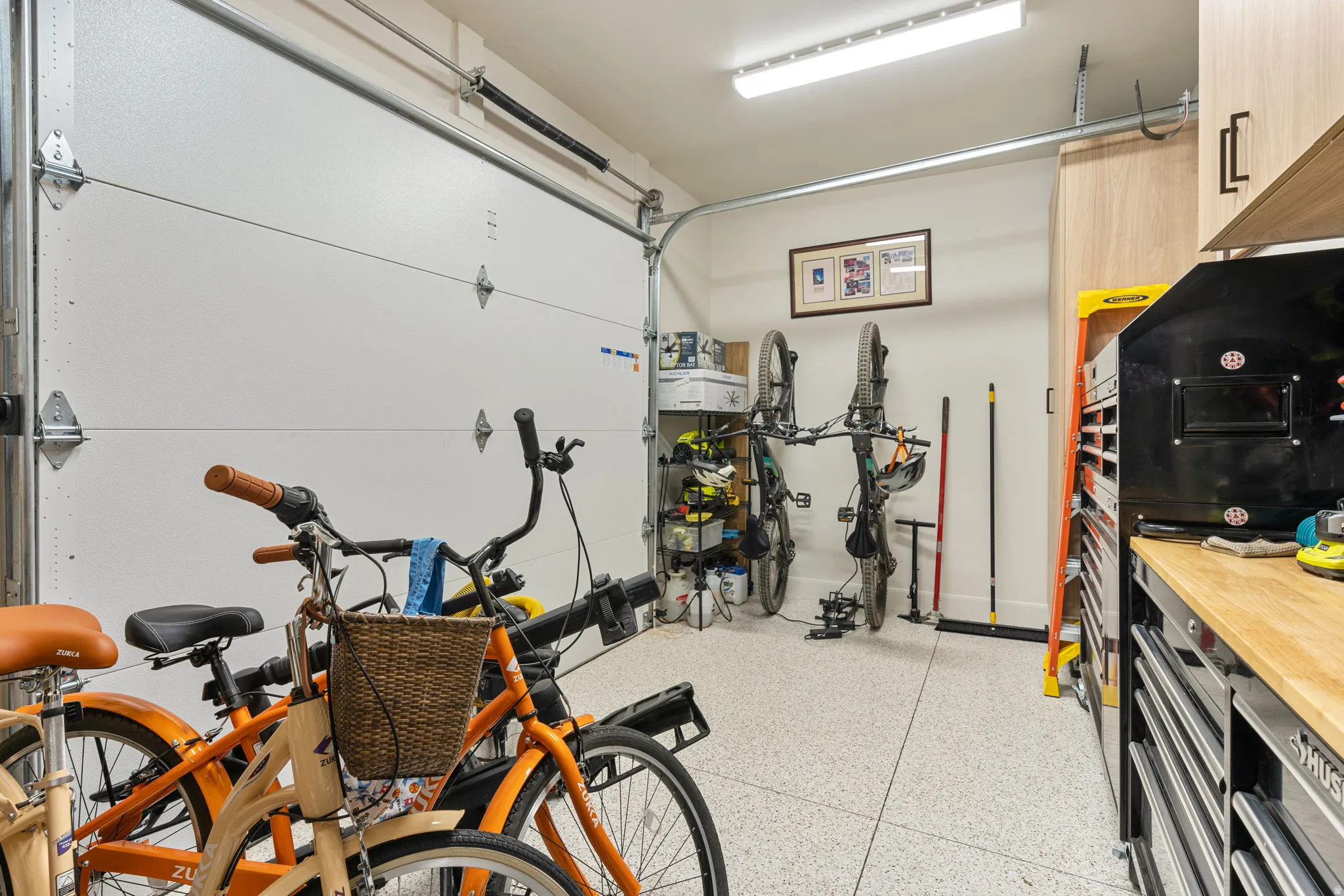 Spacious garage with epoxy flooring, white paneled garage door, built-in cabinetry, and wall-mounted storage solutions