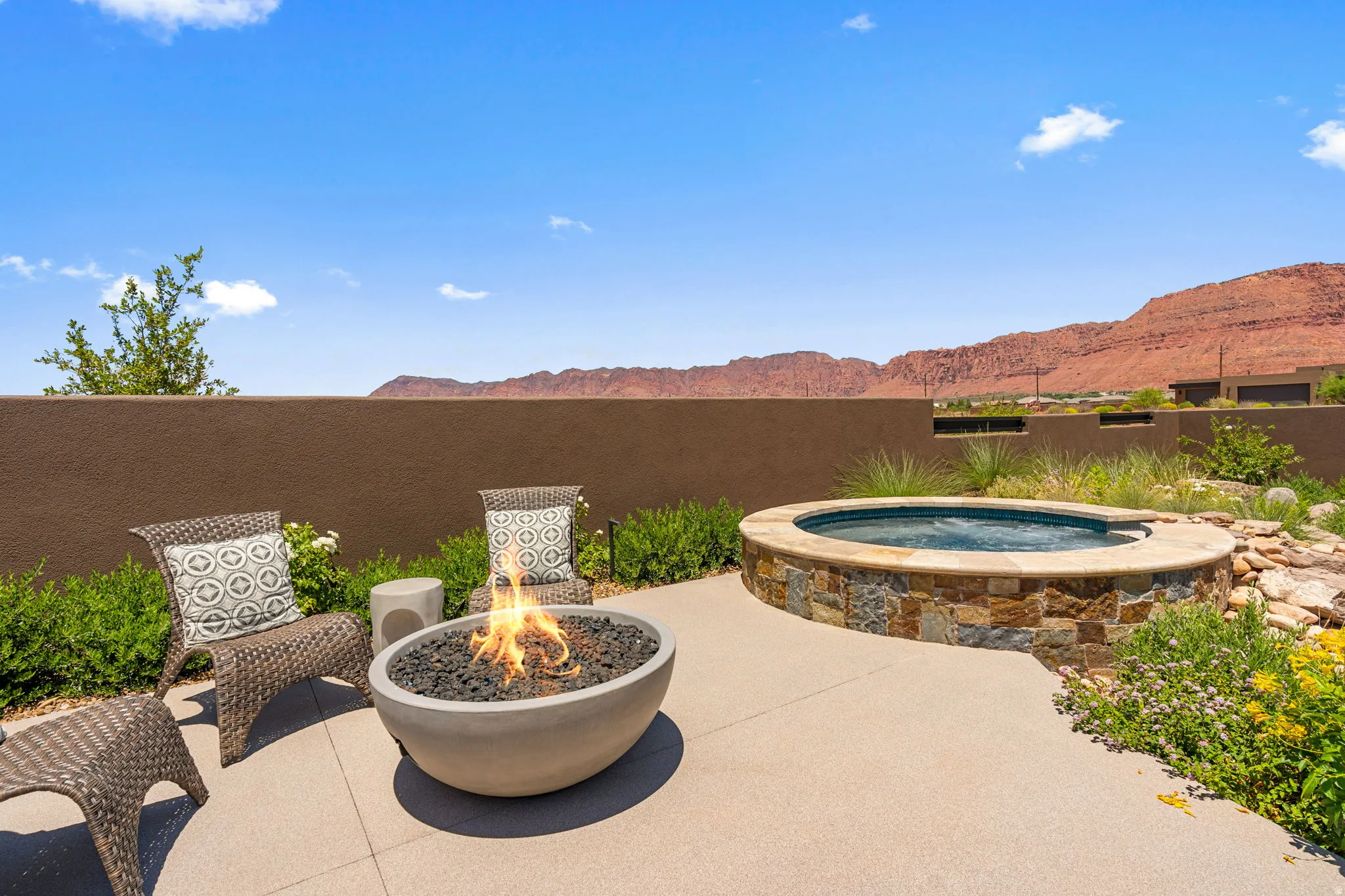 Outdoor patio featuring a stone-clad hot tub, a concrete fire pit, and a textured privacy wall