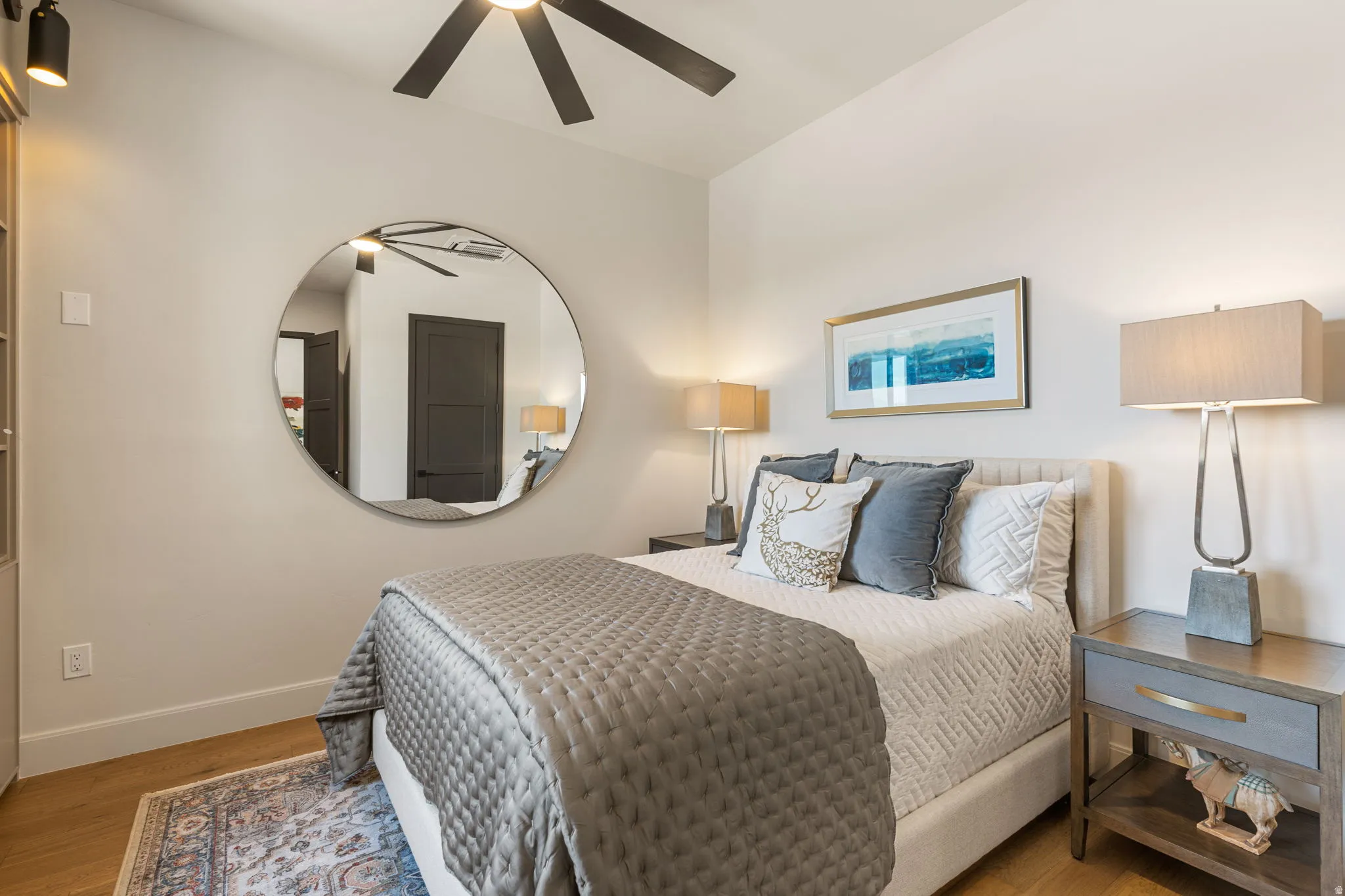 Third bedroom with hardwood flooring, a contemporary ceiling fan, and a large round wall mirror