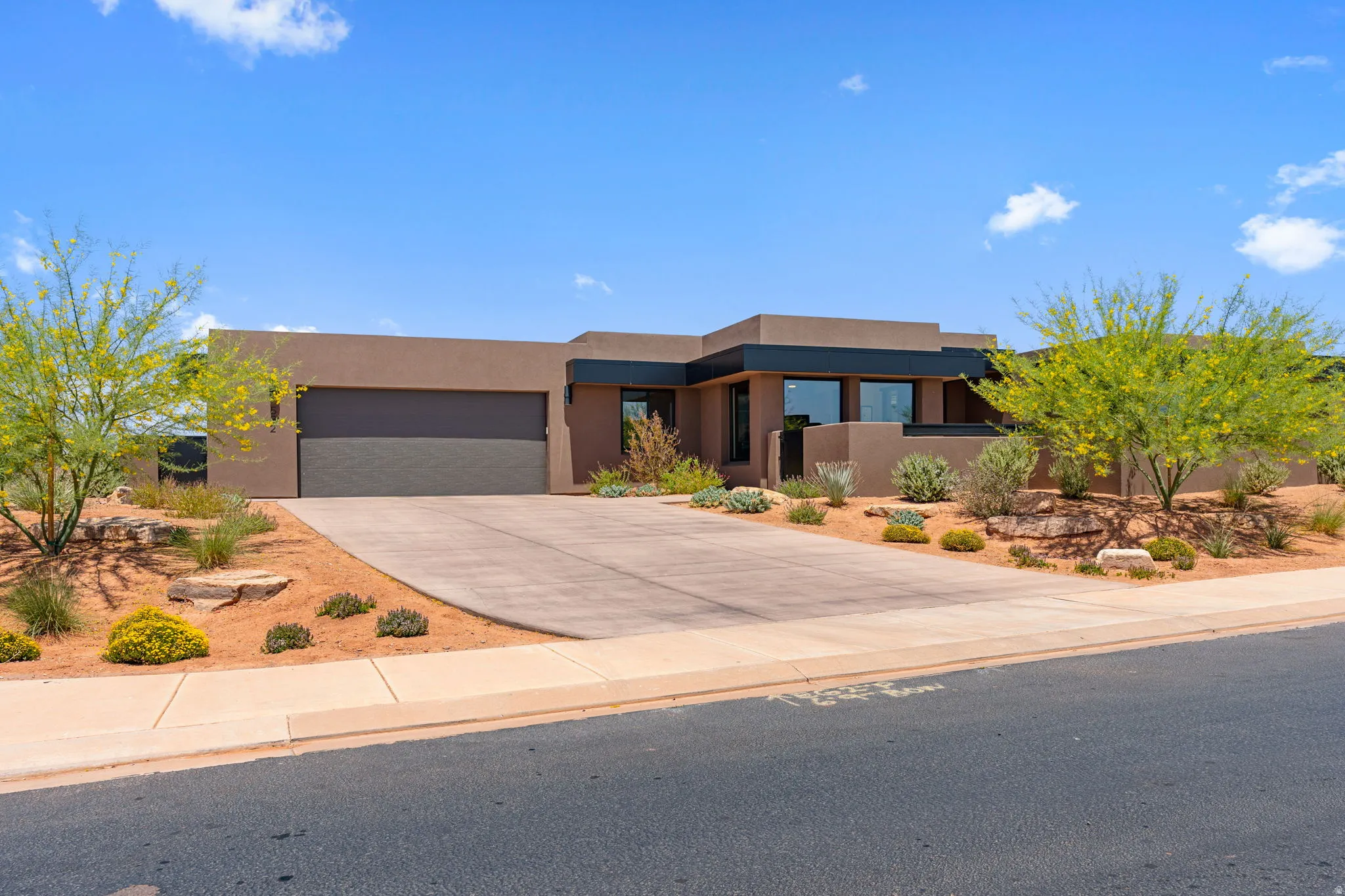 South driveway of Contemporary-style home featuring earth-toned stucco, multiple large windows, and a dark garage door