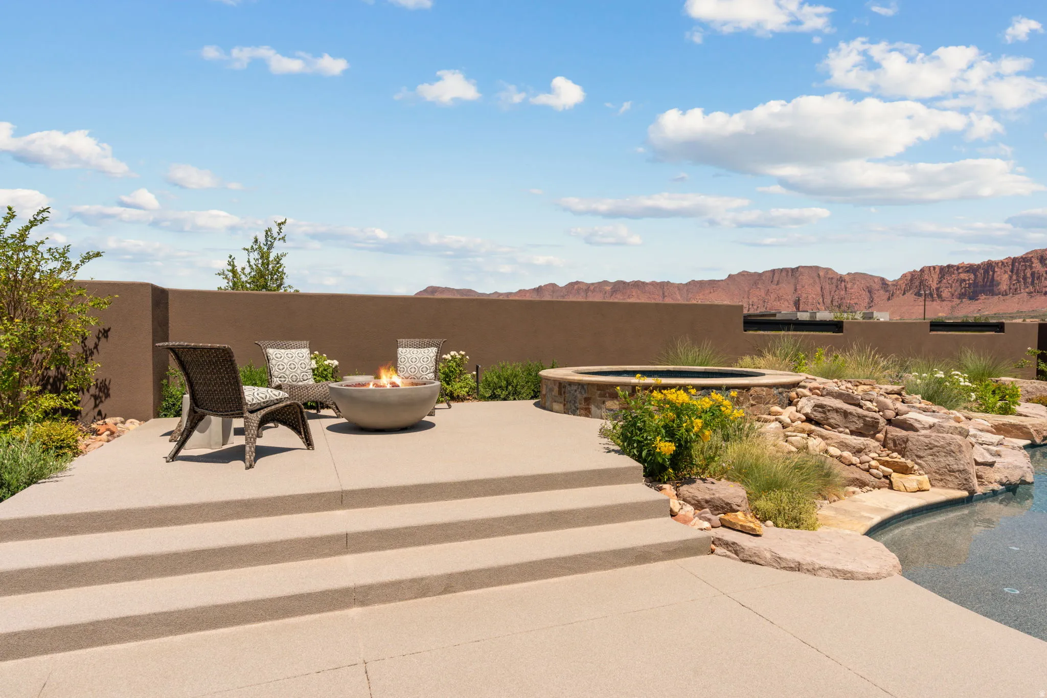 Outdoor patio featuring a built-in fire pit, multiple seating areas, a hot tub with stone surround, natural rock landscaping, and a pool with a custom edge
