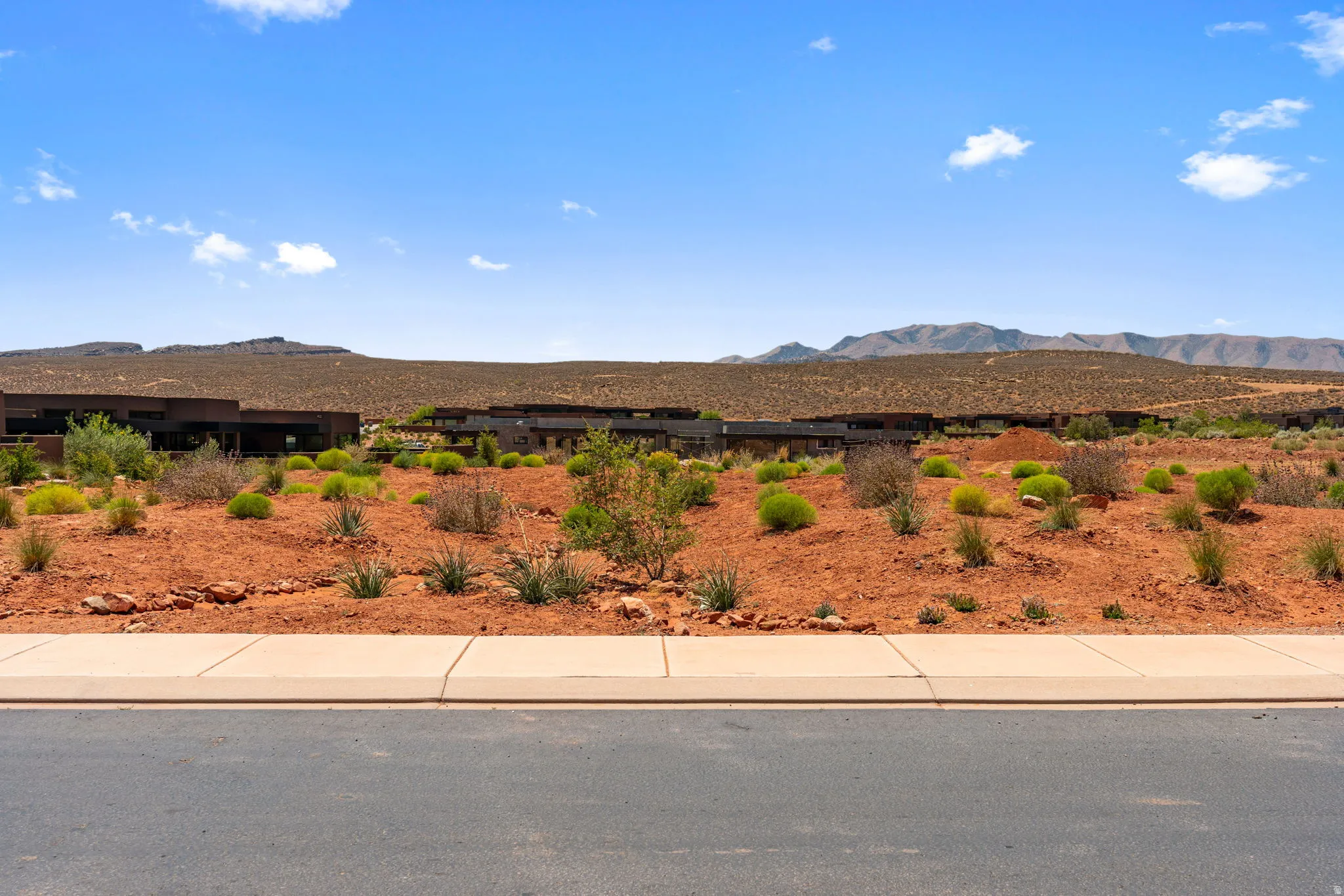 Desert landscape on view protection lot featuring red earth, scattered green vegetation, and distant mountains