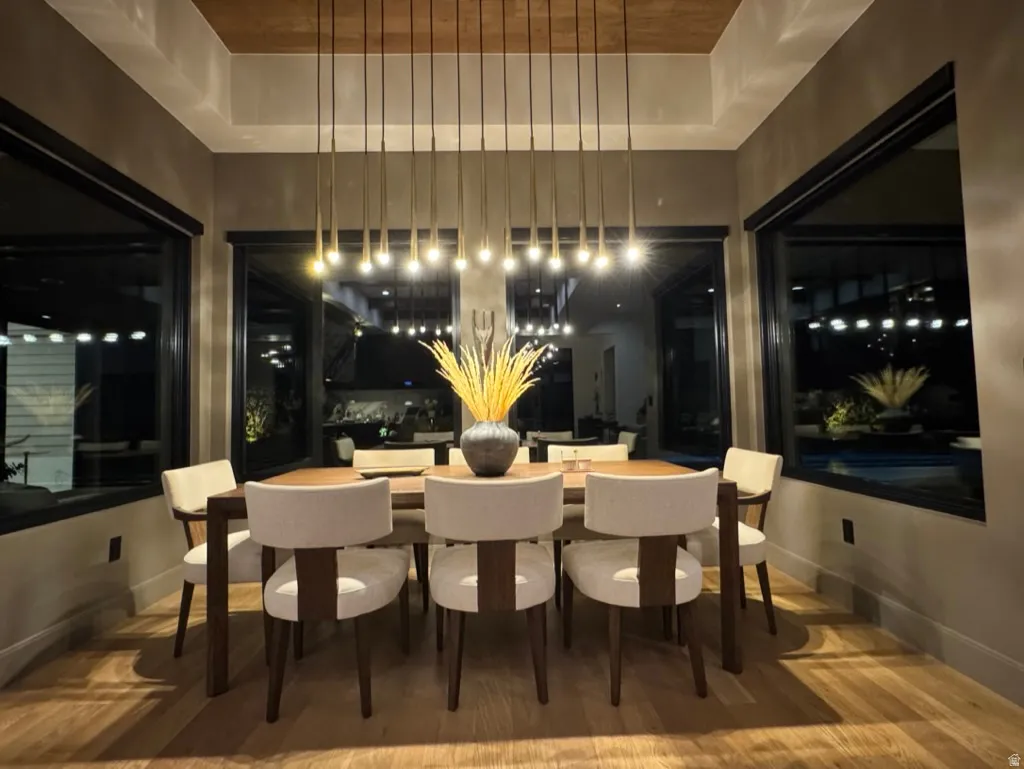 Dining area featuring hardwood flooring, a recessed ceiling with wood paneling, and a multi-pendant linear chandelier