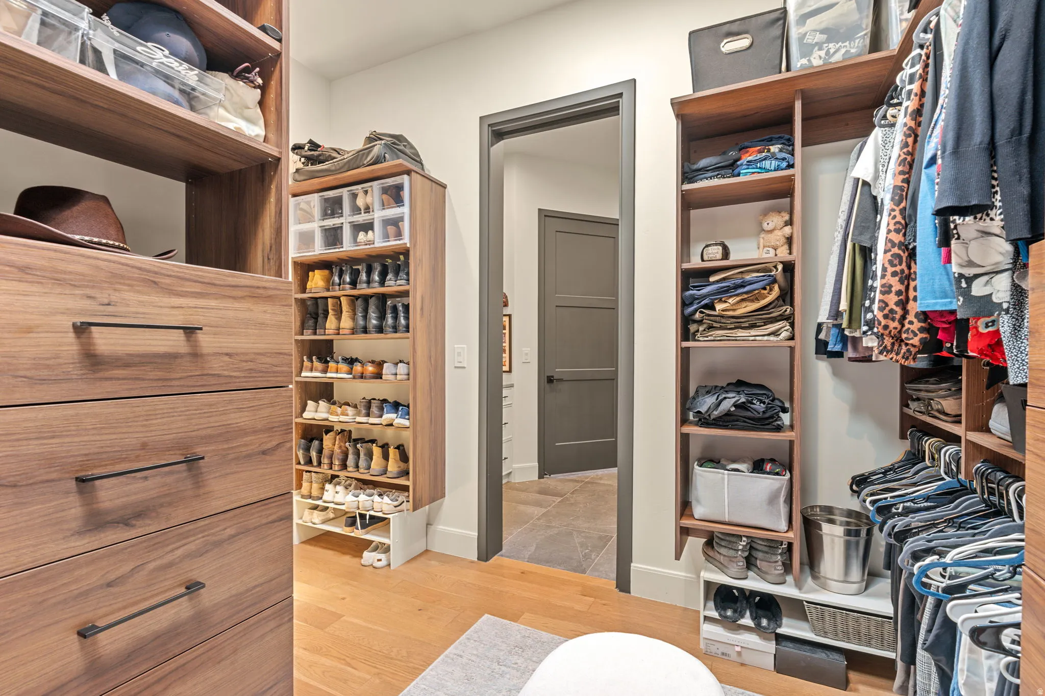 Custom closet system featuring built-in wood-finish drawers with dark hardware, integrated shelving, hardwood flooring