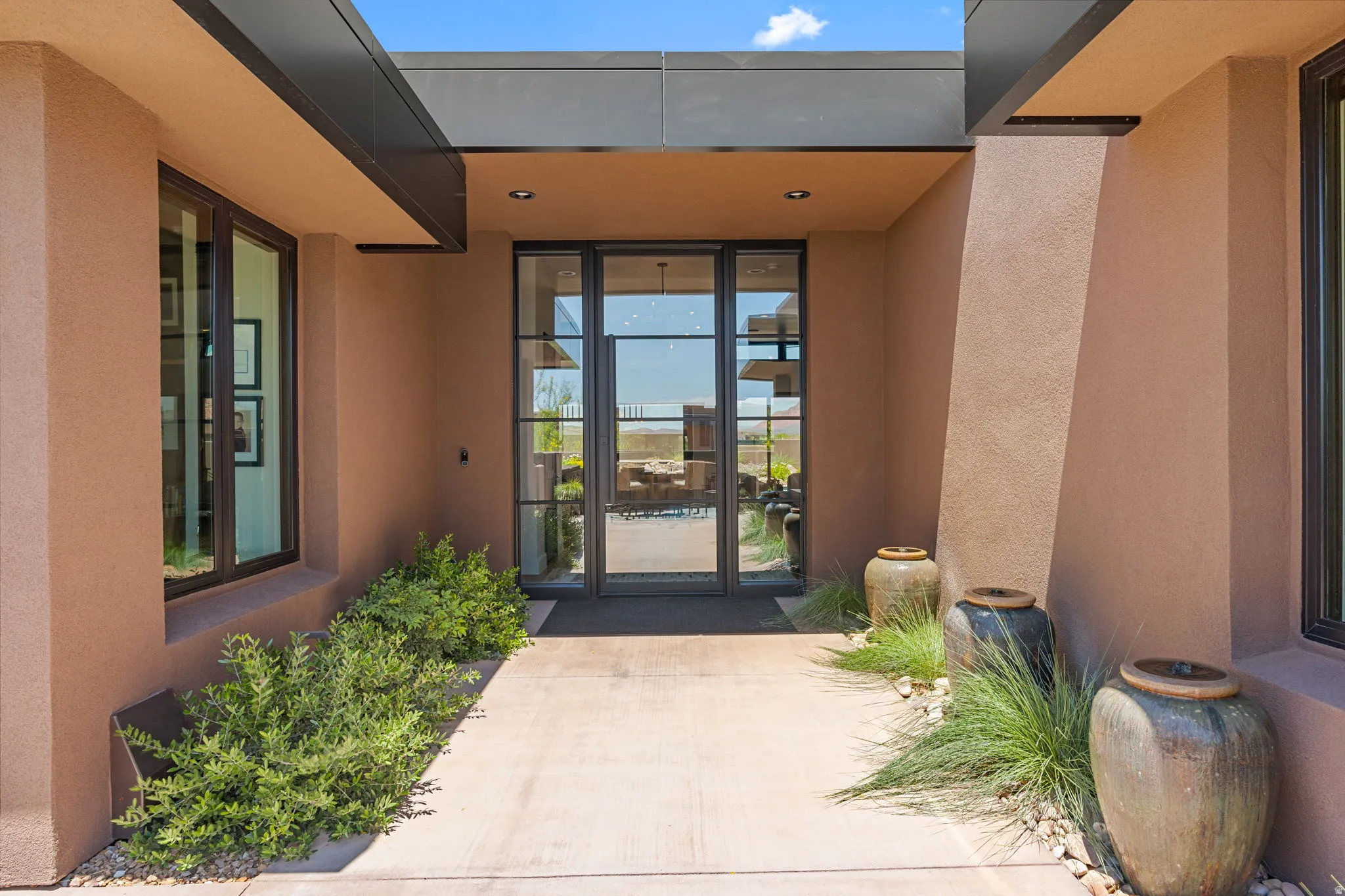 Contemporary stucco exterior featuring a large glass and metal entry door, water feature, recessed lighting, and a flat roofline