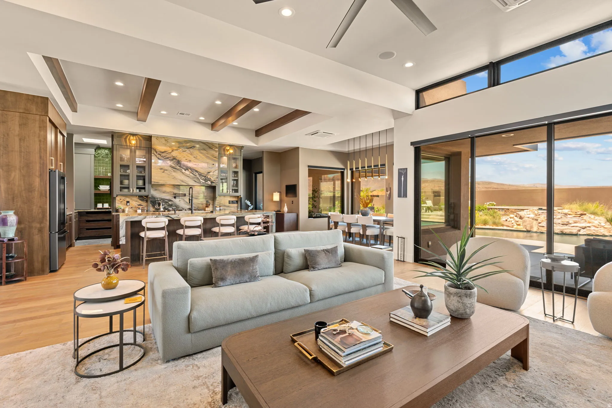 Expansive open-concept living area featuring a gourmet kitchen, exposed beam ceilings, hardwood flooring, and a wall of glass leading to outdoor space