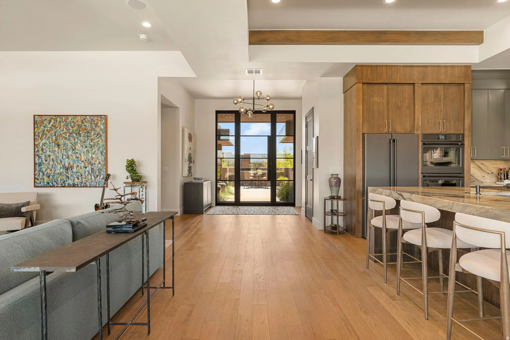Open-concept living area with hardwood flooring, a contemporary kitchen island, built-in stainless steel appliances, and a modern entry door with dark framing