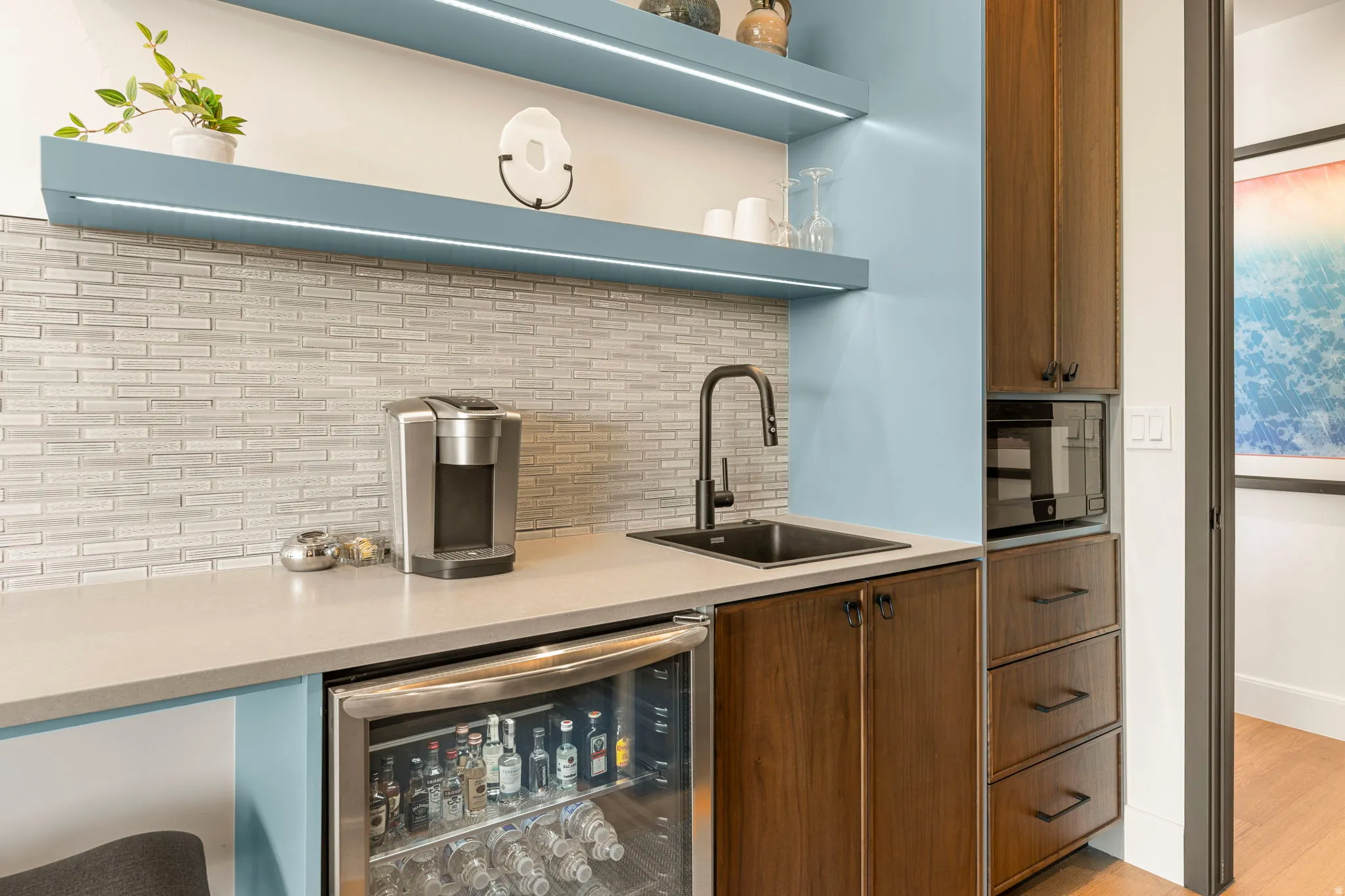 Wet bar featuring microwave, beverage fridge, wood cabinetry, light blue accent wall, and under-shelf lighting