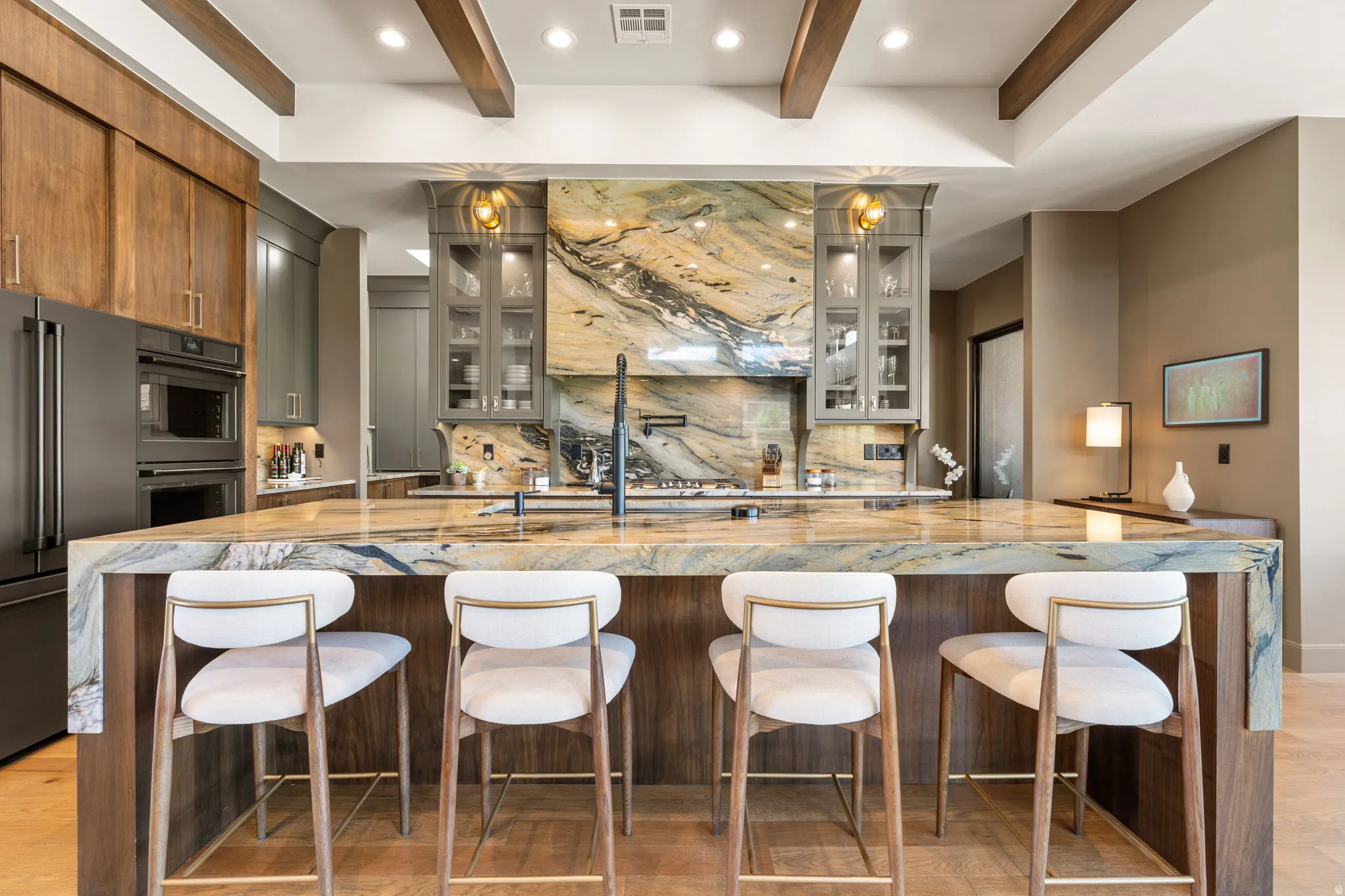 Kitchen featuring a waterfall-edge island with seating, a dramatic stone backsplash, and exposed ceiling beams