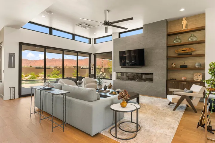 Spacious living area featuring expansive glass sliding doors, wood-finish flooring, a contemporary ceiling fan, and high transom windows