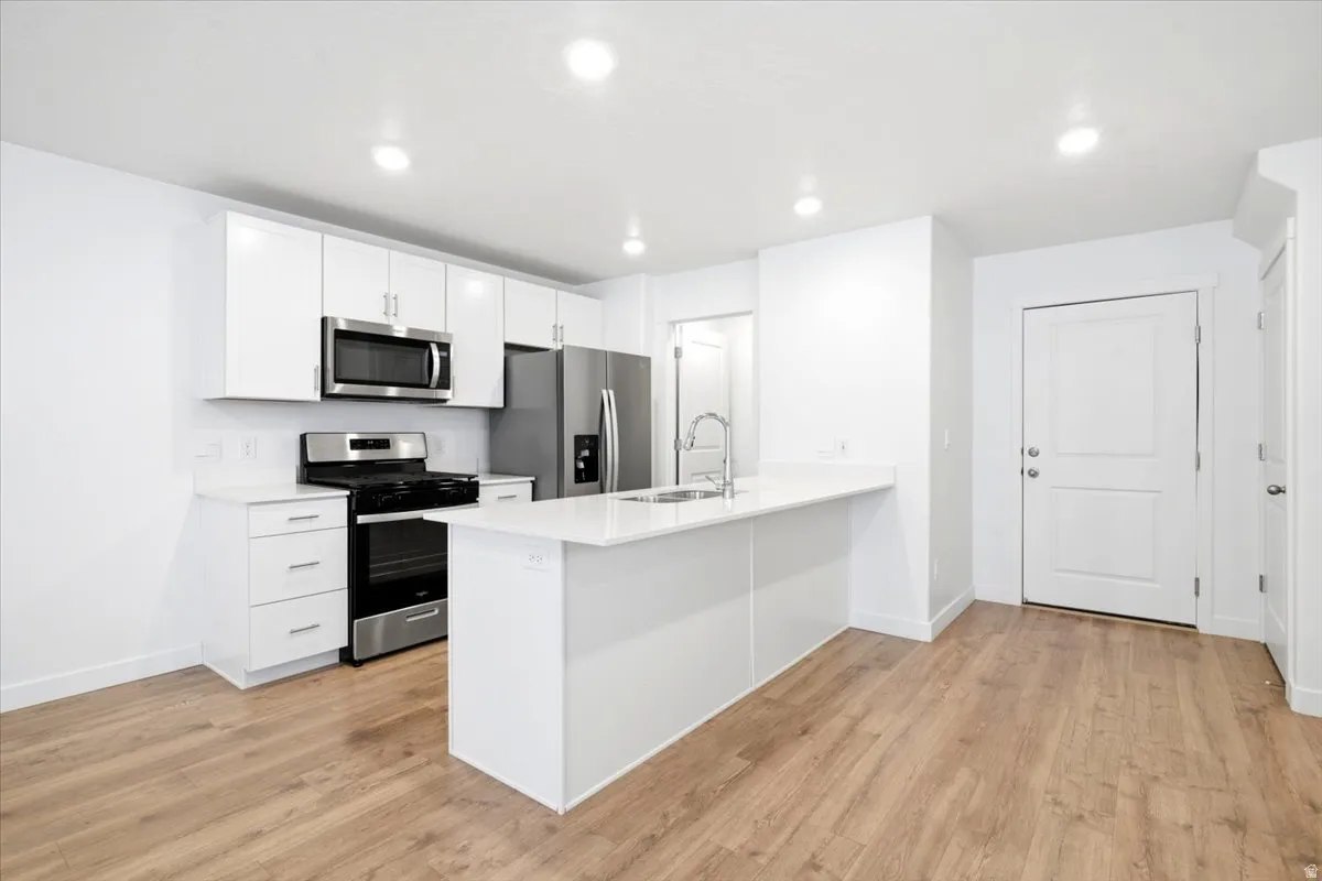 Modern kitchen featuring white cabinetry, stainless steel appliances, a center island with sink, recessed lighting
