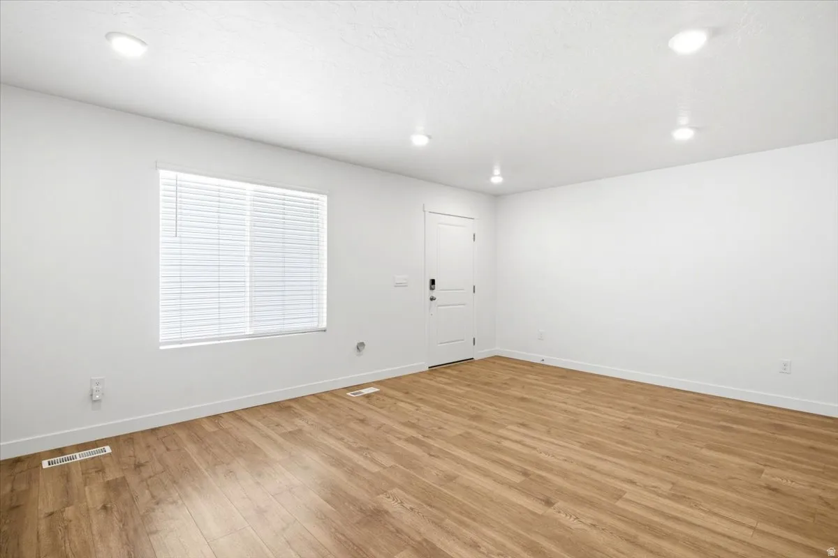 Spacious room featuring wood-finish flooring, white walls, and recessed lighting