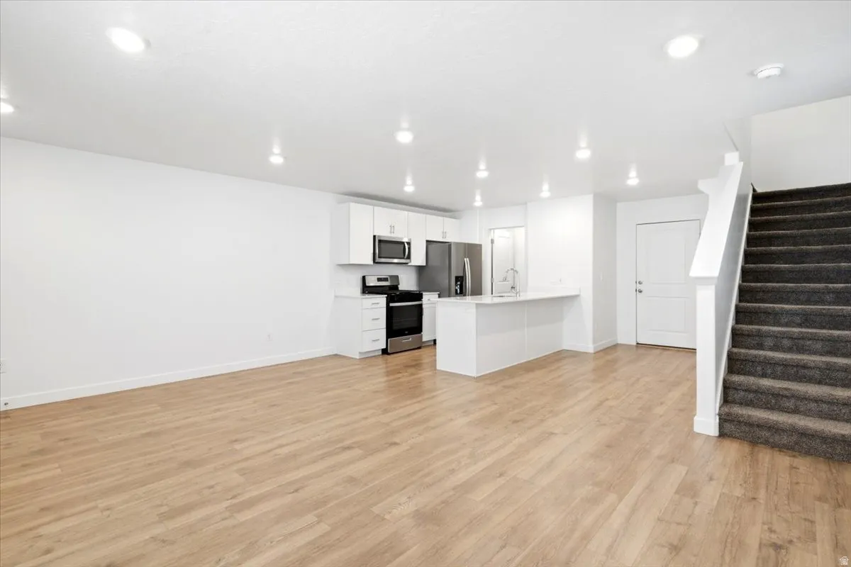 Open-concept living space featuring wood-finish flooring, recessed lighting, and a white kitchen with stainless steel appliances