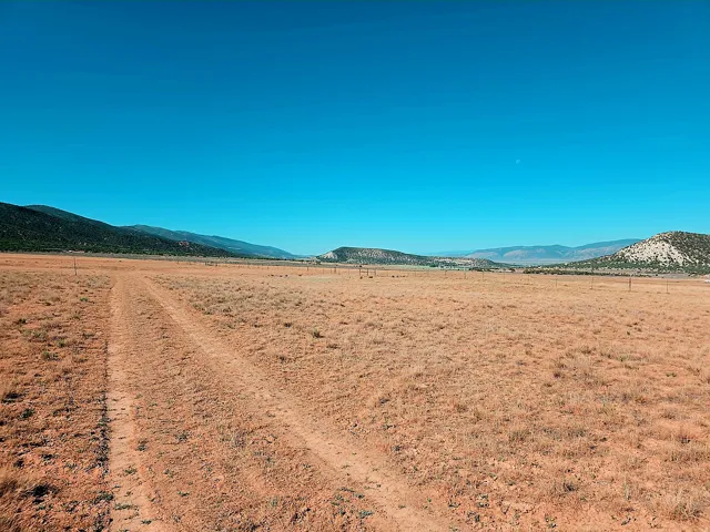 Expansive open land featuring a clear blue sky, distant mountains, and a natural dirt path