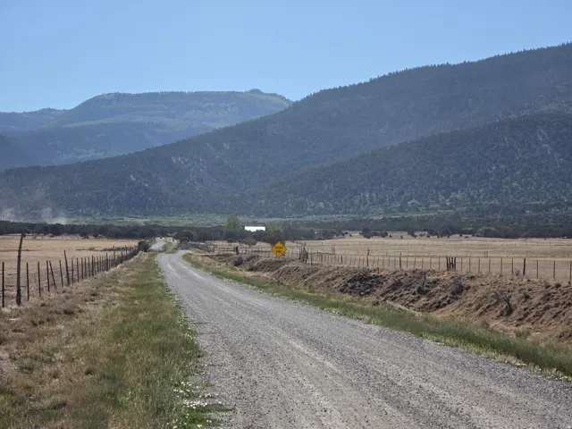 Gravel road extending through open fields with distant mountainous terrain