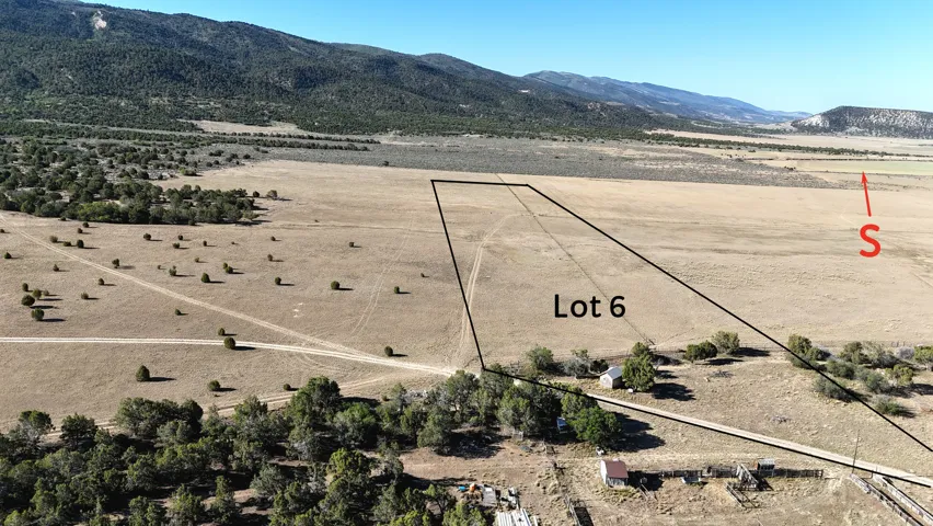 Expansive Lot 6 featuring open fields, scattered natural vegetation, and distant mountain ranges
