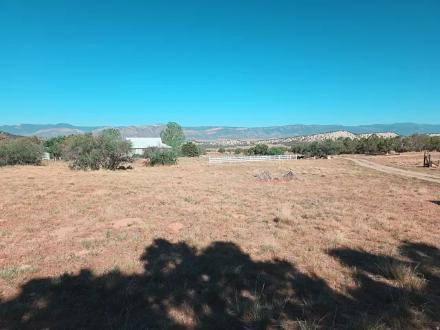 Expansive open land featuring distant mountain ranges and a partially visible white farmhouse