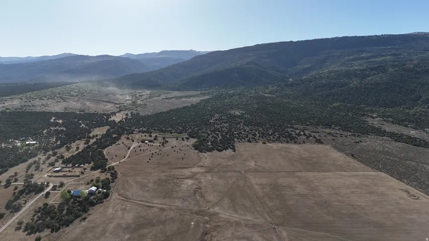 Expansive rural property featuring a large open field, surrounded by extensive natural foliage and distant mountain ranges