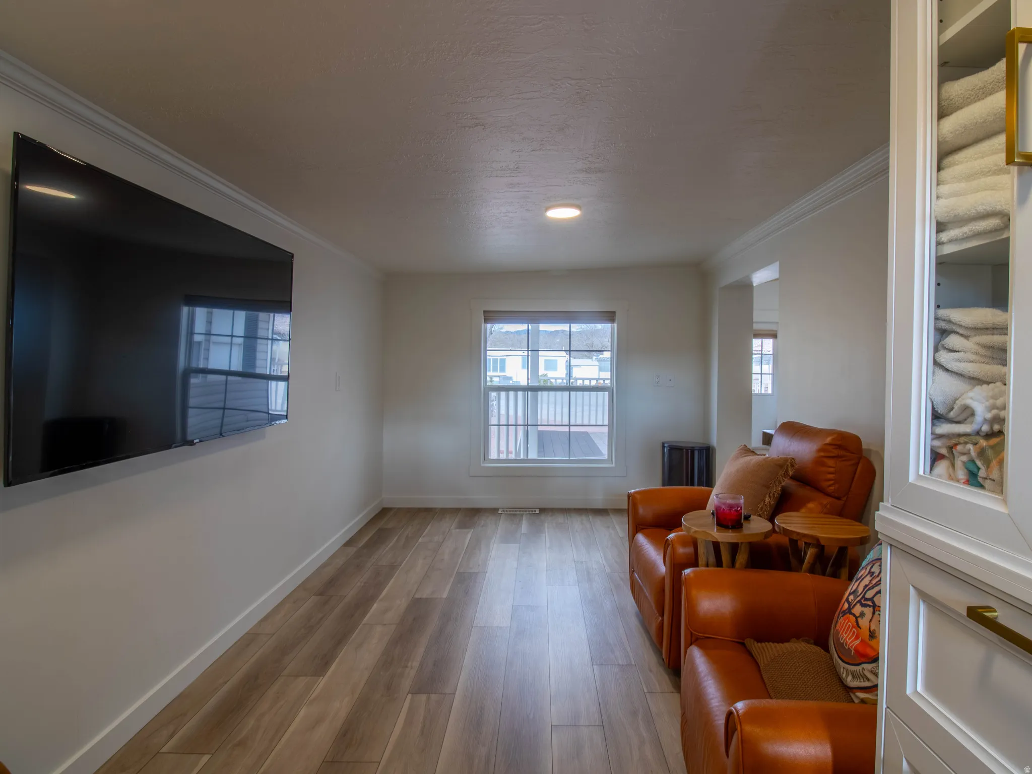 Living area featuring wood-finish flooring, recessed lighting, white trim, a mounted television, and a window with a white frame