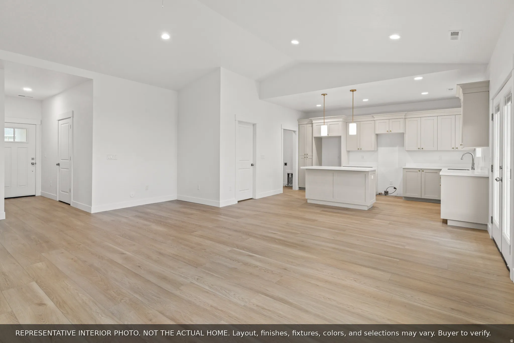 Open-concept living area featuring wood-finish flooring, a kitchen island with pendant lighting, white shaker-style cabinetry, and white subway tile backsplash