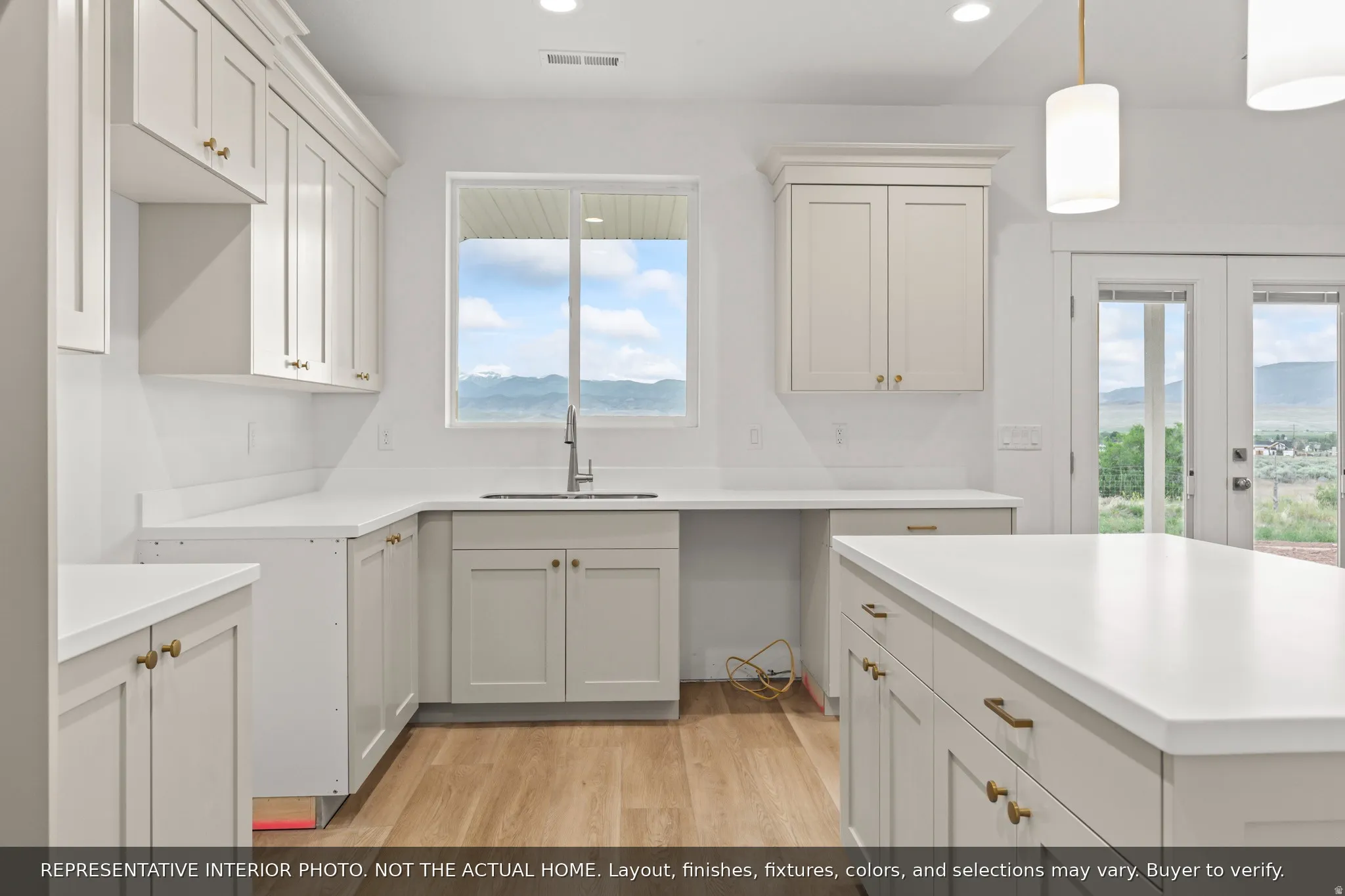 White kitchen cabinetry with brass hardware, a central kitchen island, wood-finish flooring, and a stainless-steel sink with a window above