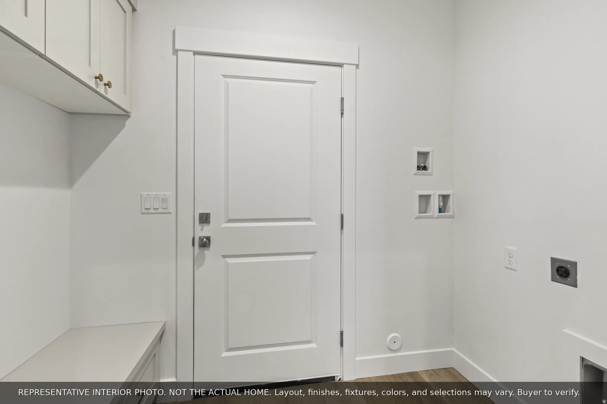 White flat panel cabinetry with brass hardware, built-in bench seating, wood-finish flooring, and white interior door with contemporary hardware