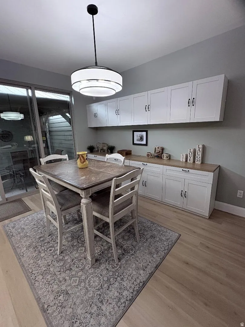 Dining area featuring wood-finish flooring, a contemporary ceiling light fixture, and extensive white cabinetry with wood-finish countertops