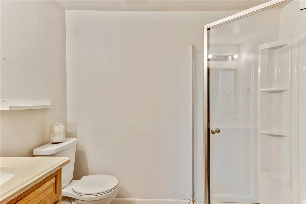 Bathroom featuring a standing shower with clear glass enclosure and built-in shelving, a toilet, and a vanity with a light-colored countertop and wood-finish cabinetry