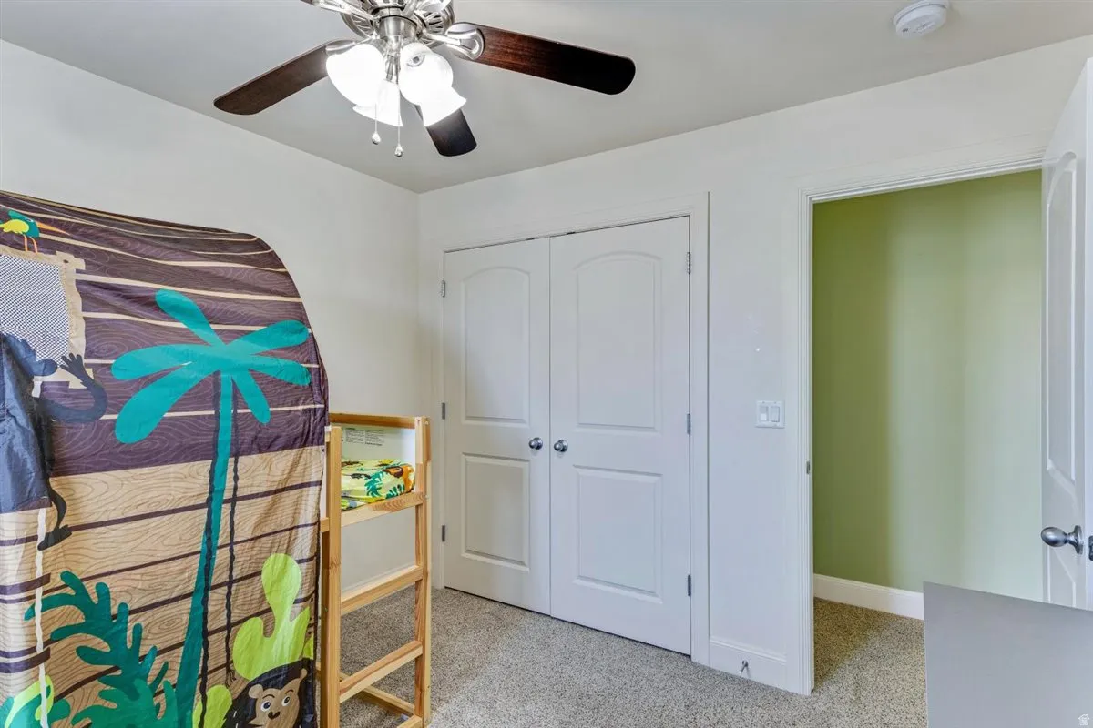 Bedroom featuring neutral carpeting, a ceiling fan with integrated lighting, and white bi-fold closet doors