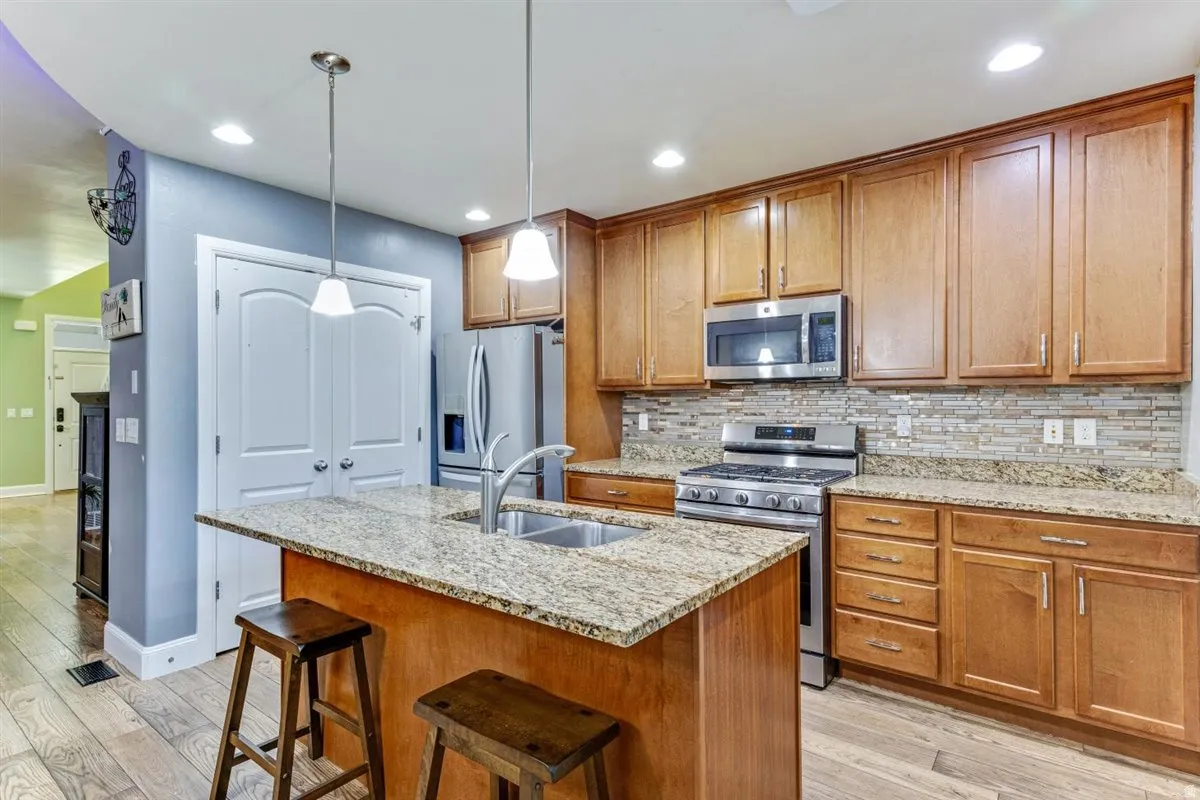 Kitchen featuring a central island with a double basin sink, granite countertops, wood-finish flooring, stainless steel appliances, and wood cabinetry