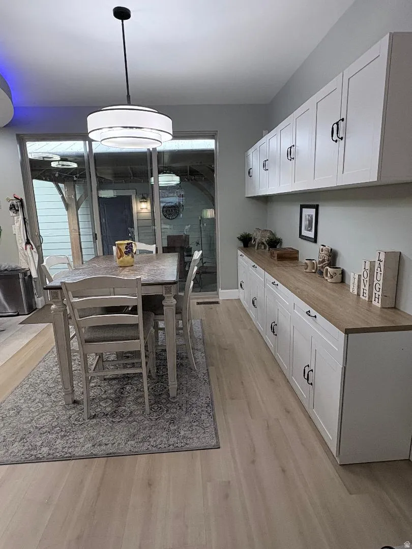 Open concept area featuring light wood-finish flooring, white shaker-style cabinetry with matte black hardware, and a wood-finish countertop