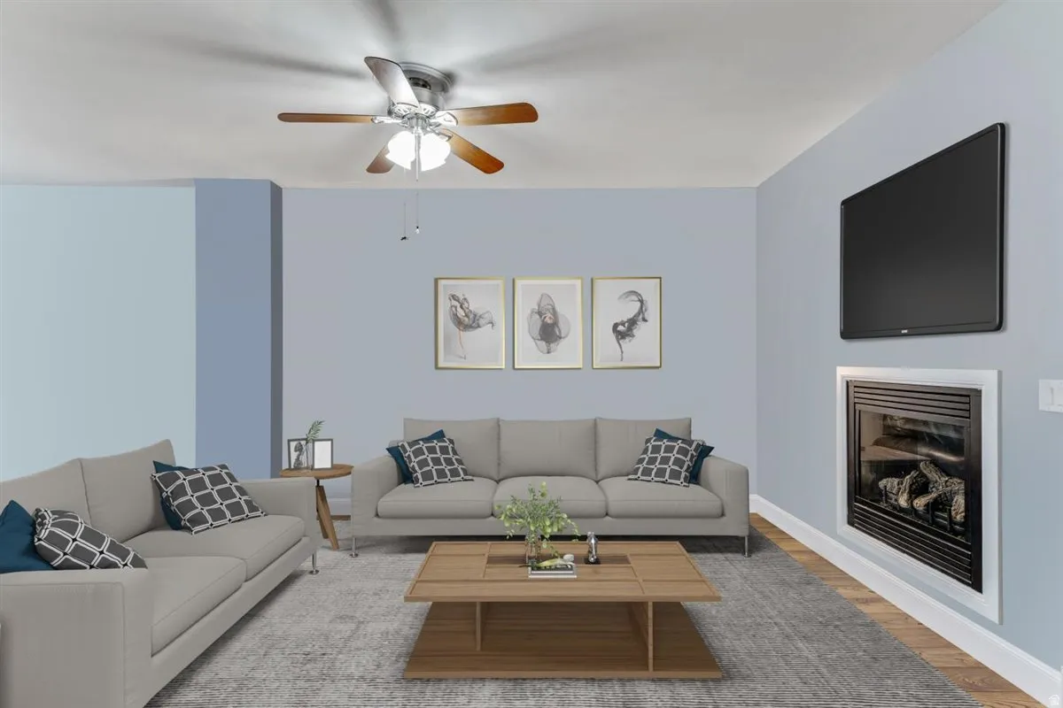 Living area featuring light blue wall colors, wood-finish flooring, a ceiling fan with light fixture, and an inset fireplace with a white surround