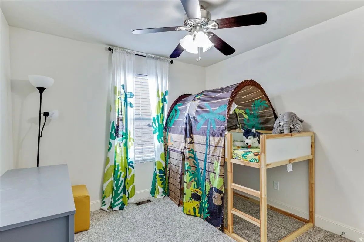 Bedroom featuring light gray carpet flooring, a ceiling fan with integrated lighting, and a window with blinds