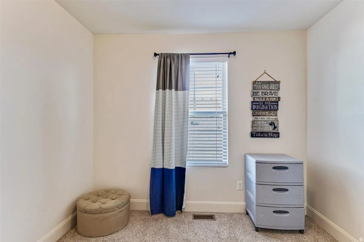 Inviting room featuring a window with blinds, light-colored walls, and neutral carpeting