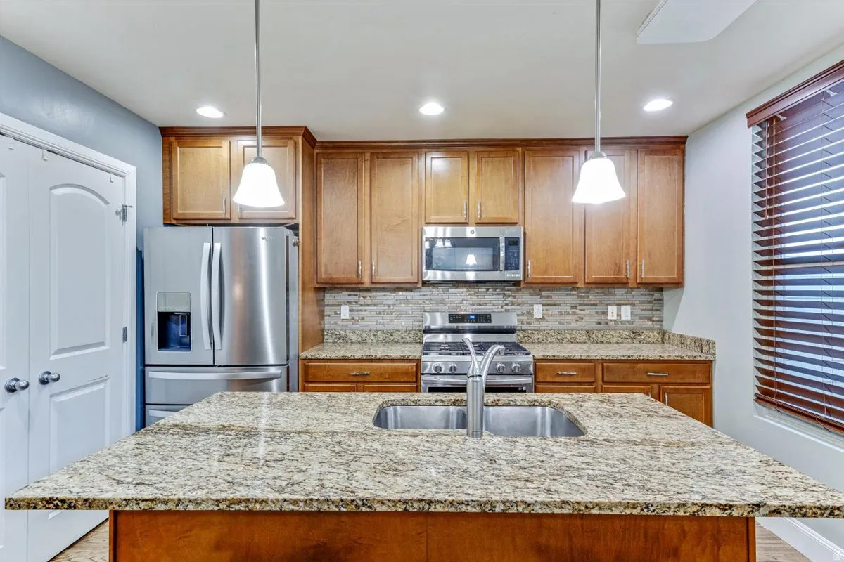 Kitchen featuring a large island with an undermount double basin stainless steel sink, granite countertops, wood cabinetry, and stainless steel appliances
