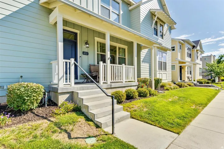 Inviting exterior featuring a light blue siding, a covered porch with white railings, a dark blue front door, concrete steps with a black handrail, and a manicured lawn