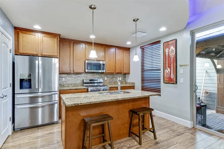 Kitchen featuring wood-finish flooring, stainless steel appliances, granite countertops, a tiled backsplash, and recessed lighting