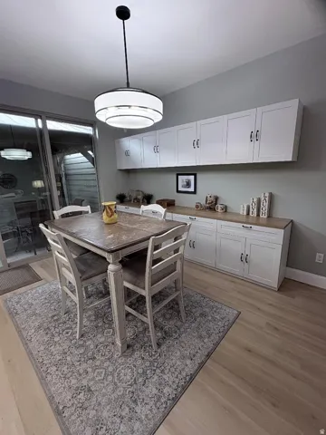 Dining area featuring wood-finish flooring, a contemporary ceiling light fixture, and extensive white cabinetry with wood-finish countertops